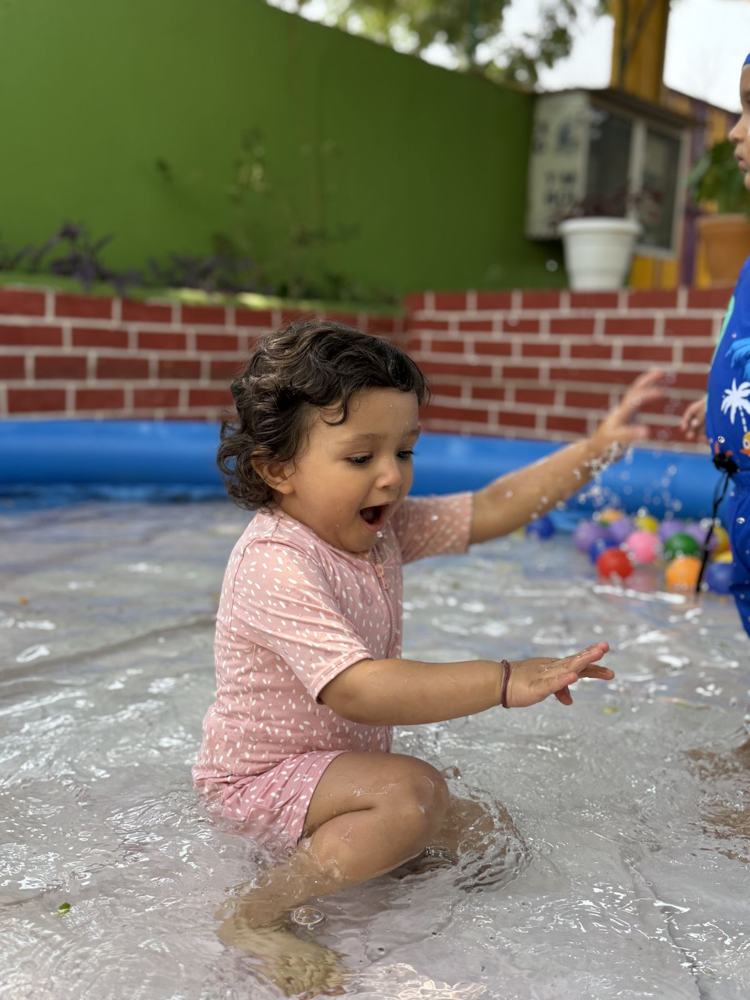 A toddler laughing while splashing in a water pool