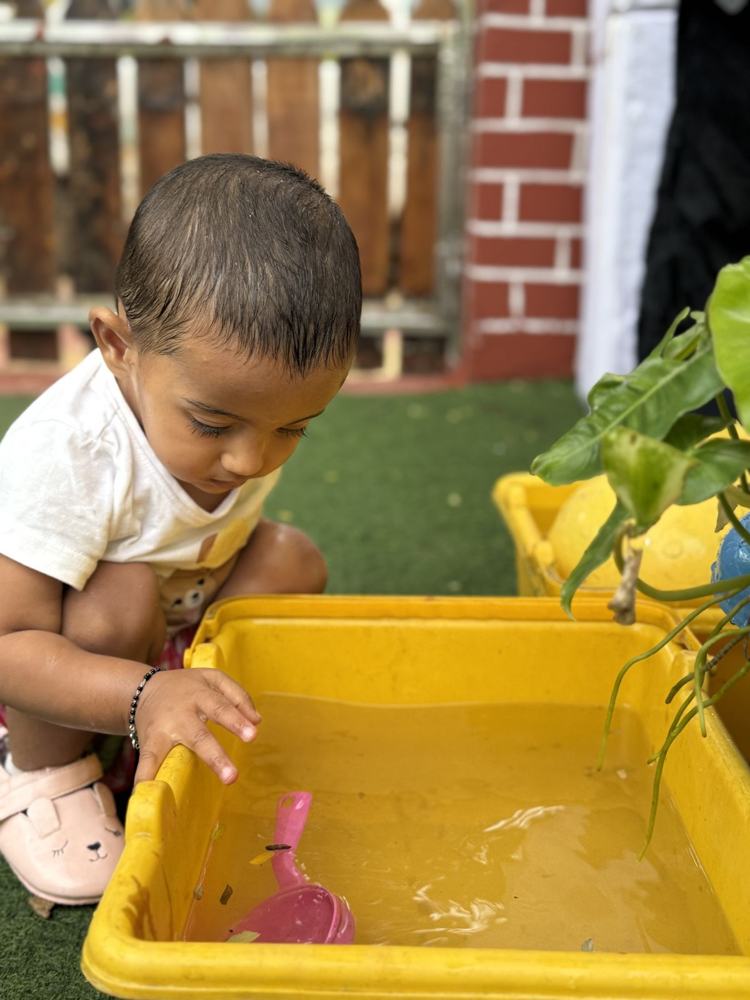 A toddler scooping water in a yellow tub